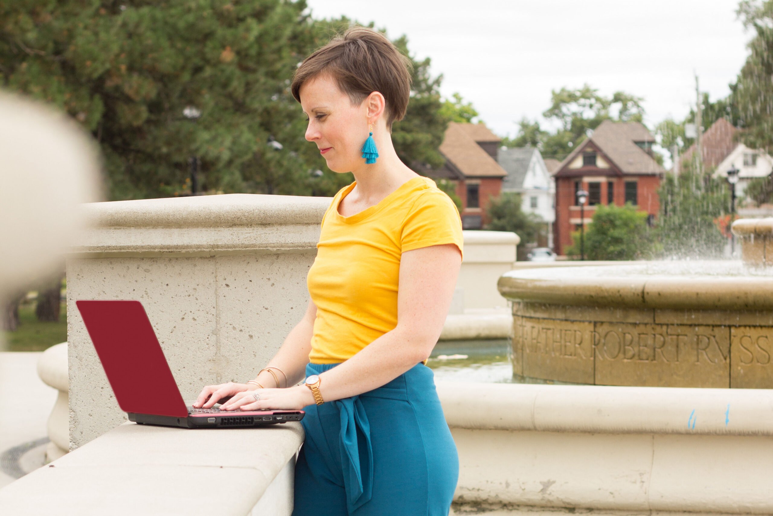 woman leaning on concrete pillar typing on laptop