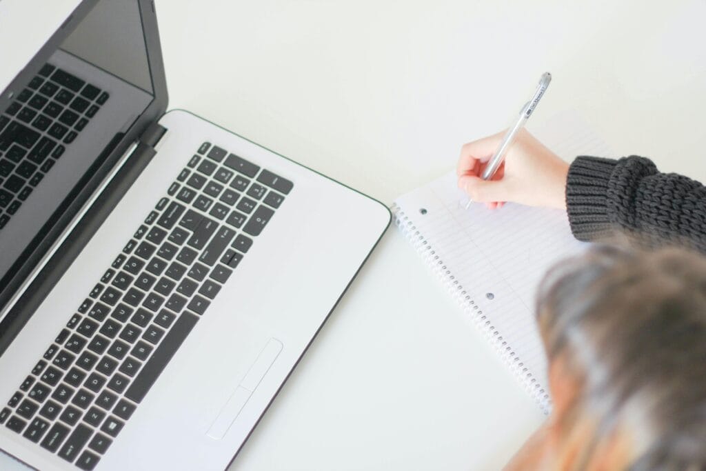 woman writing on paper near a laptop