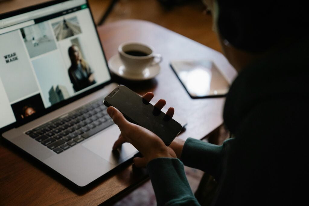 girl holding mobile phone looking at laptop