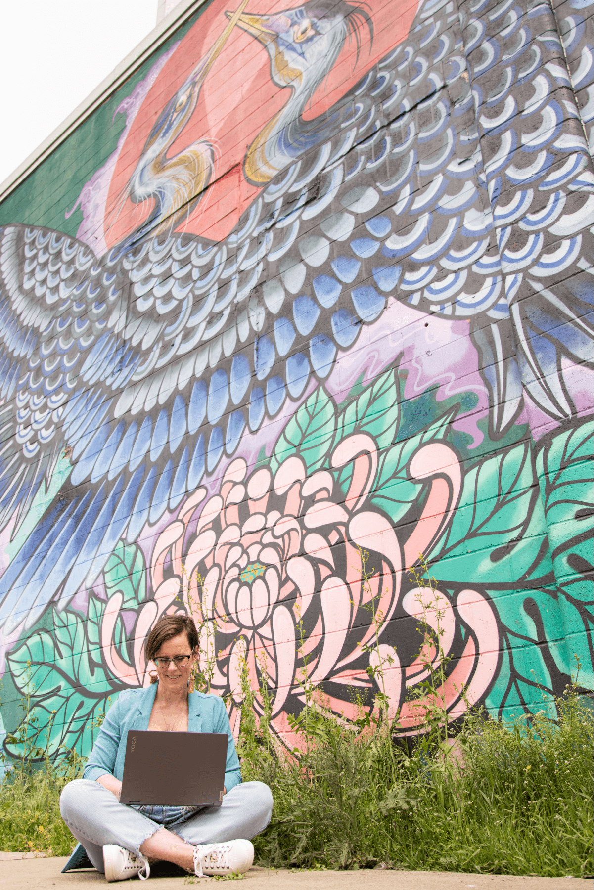 sarah mckenzie sitting with laptop in front of a graffiti wall