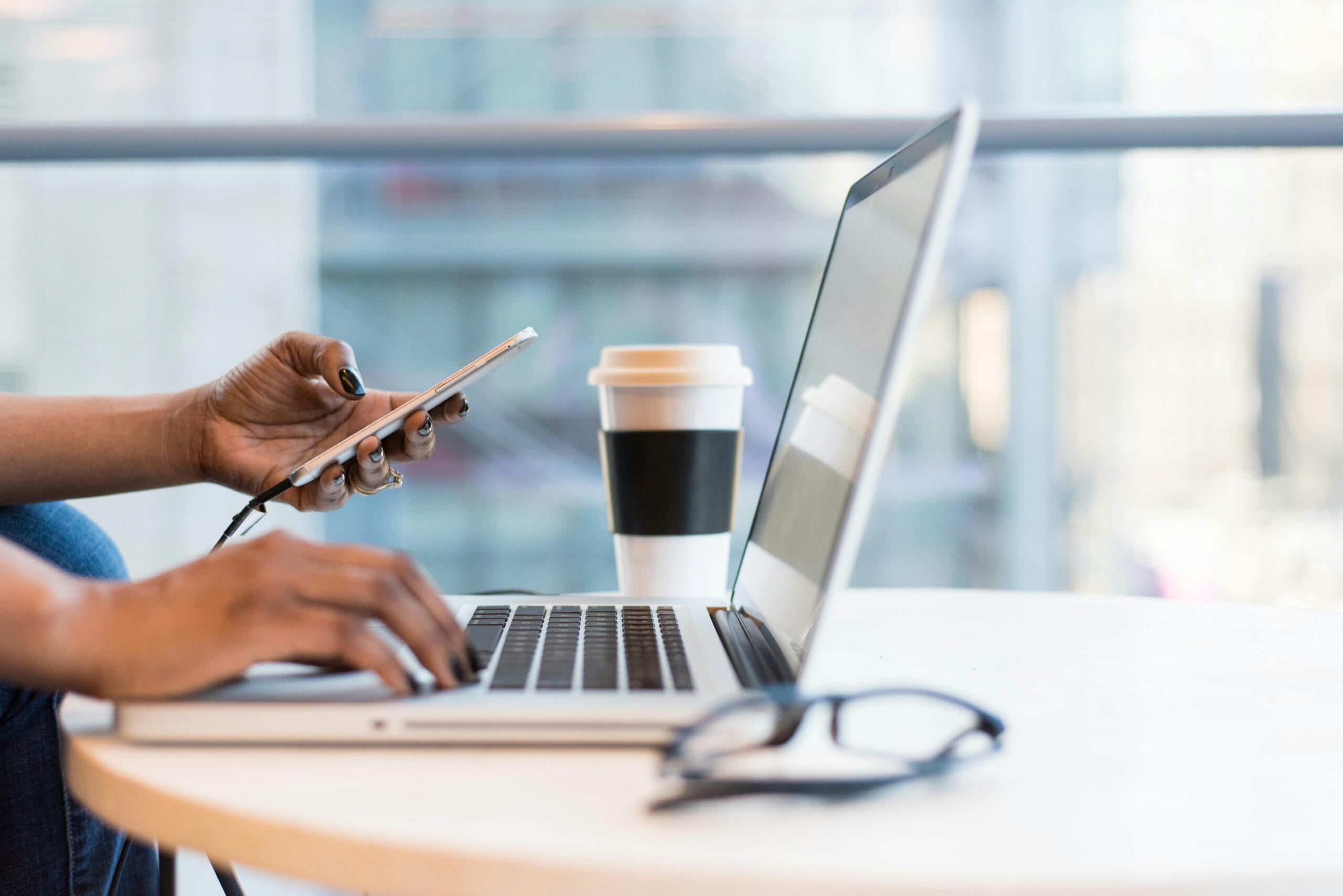 female hands typing on a laptop and holding a mobile phone