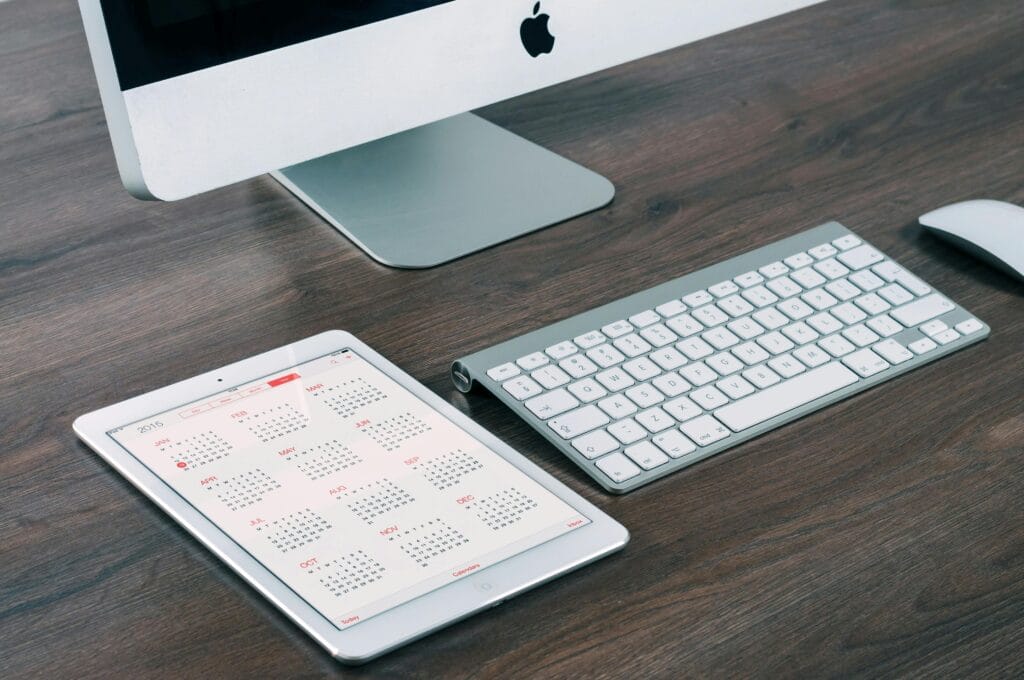 image of computer on a desk with an ipad showing a calendar