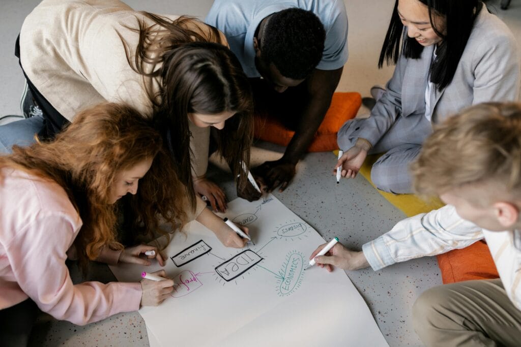 team of people writing on a paper that says "IDEA" on the floor