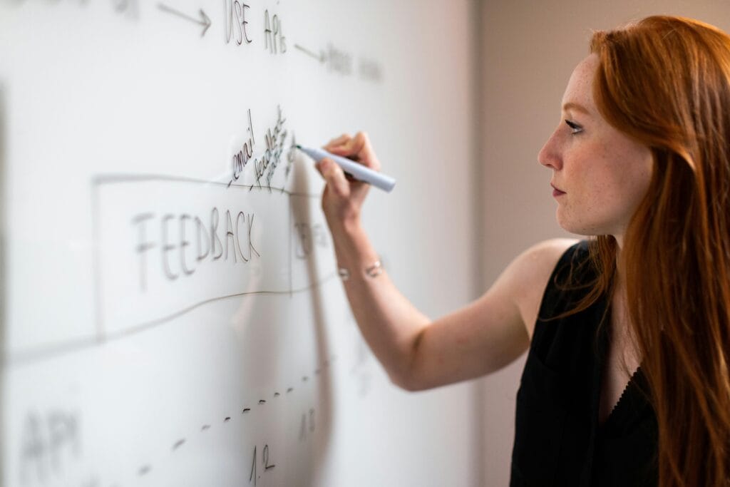red-haired woman writing "Feedback" on a white board
